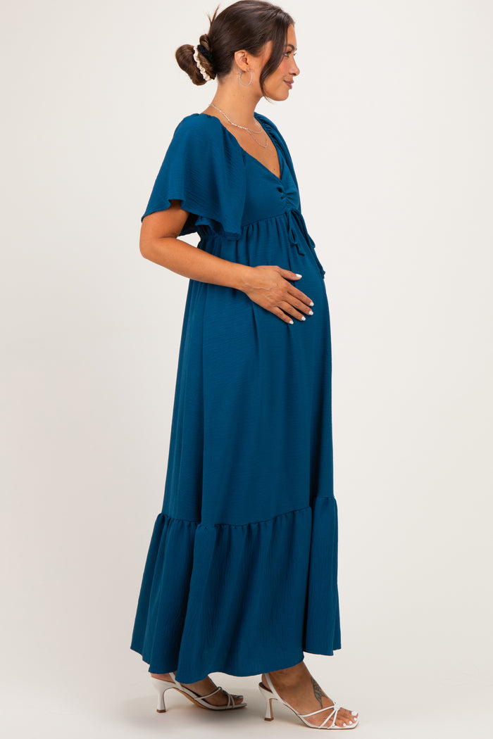 woman wearing a teal maternity maxi dress with flutter sleeves and a baby bump visible