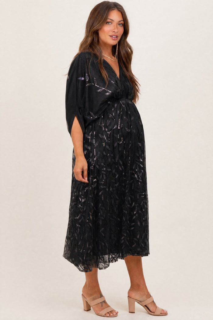 woman wearing a black maternity dress with a flowing design and sheer overlay, showcasing her baby bump