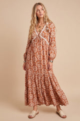 woman wearing a brown patterned maxi dress with long sleeves and a tiered skirt, styled with accessories