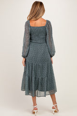 woman wearing a teal maternity dress with puff sleeves and a tiered skirt, showing a subtle baby bump
