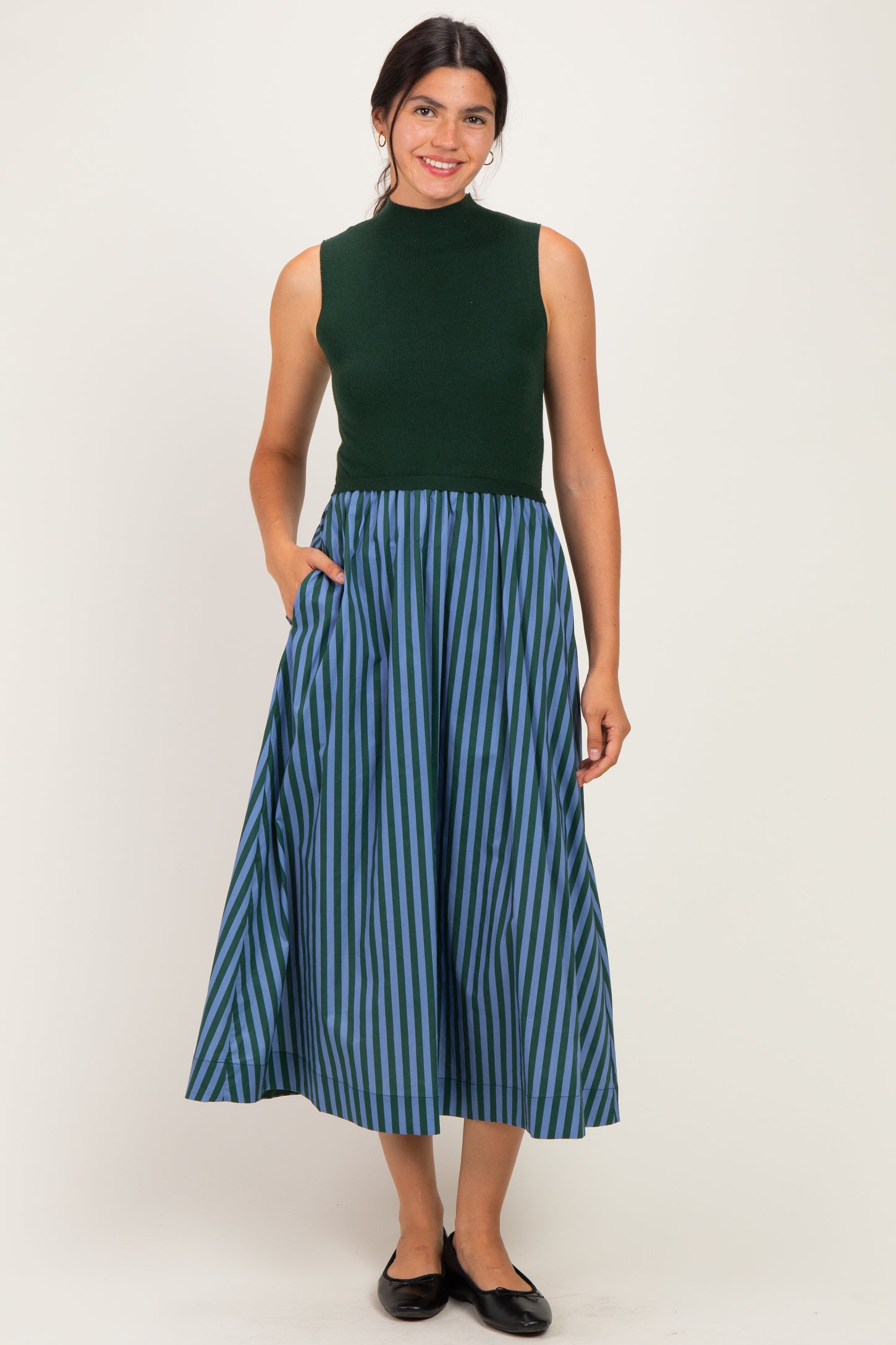 woman wearing a sleeveless green knit top and a long blue and green striped skirt with pockets
