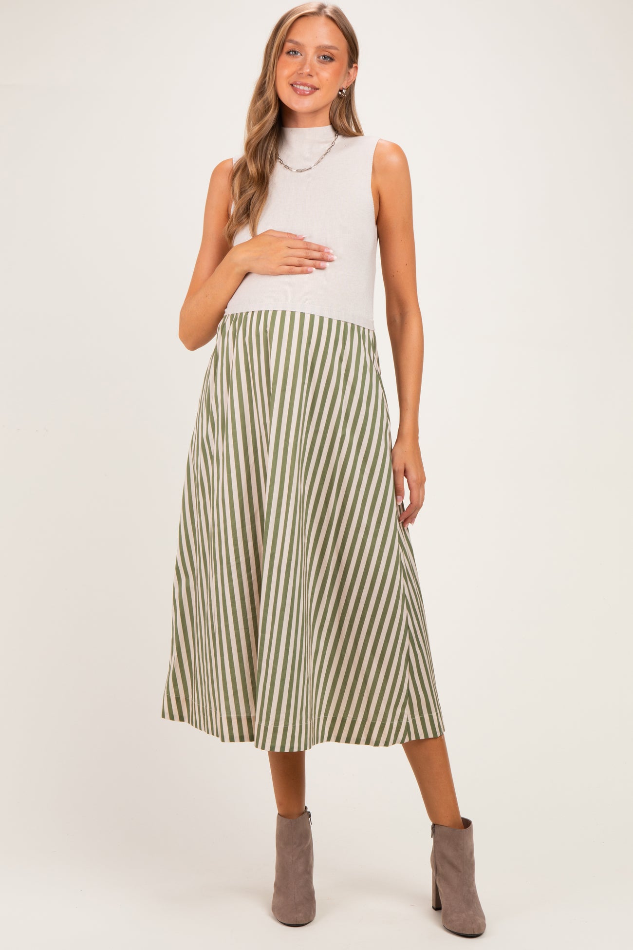 woman wearing a sleeveless grey mock neck maternity dress with green and white stripes and holding her baby bump