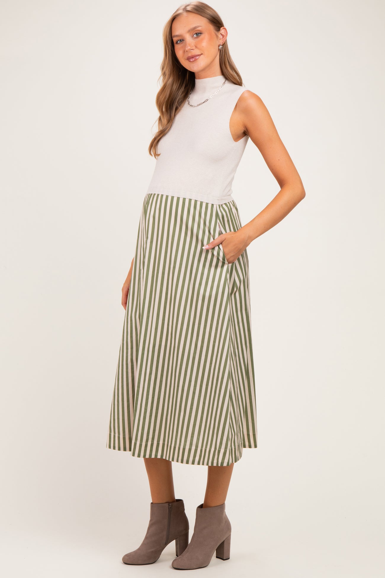 woman wearing a light gray sleeveless top and a green and white striped maternity skirt with pockets, baby bump visible