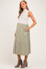 woman wearing a light gray sleeveless top and a green and white striped maternity skirt with pockets, baby bump visible
