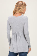 women wearing a grey long sleeve top with a flared back and pleated detail, viewed from the back
