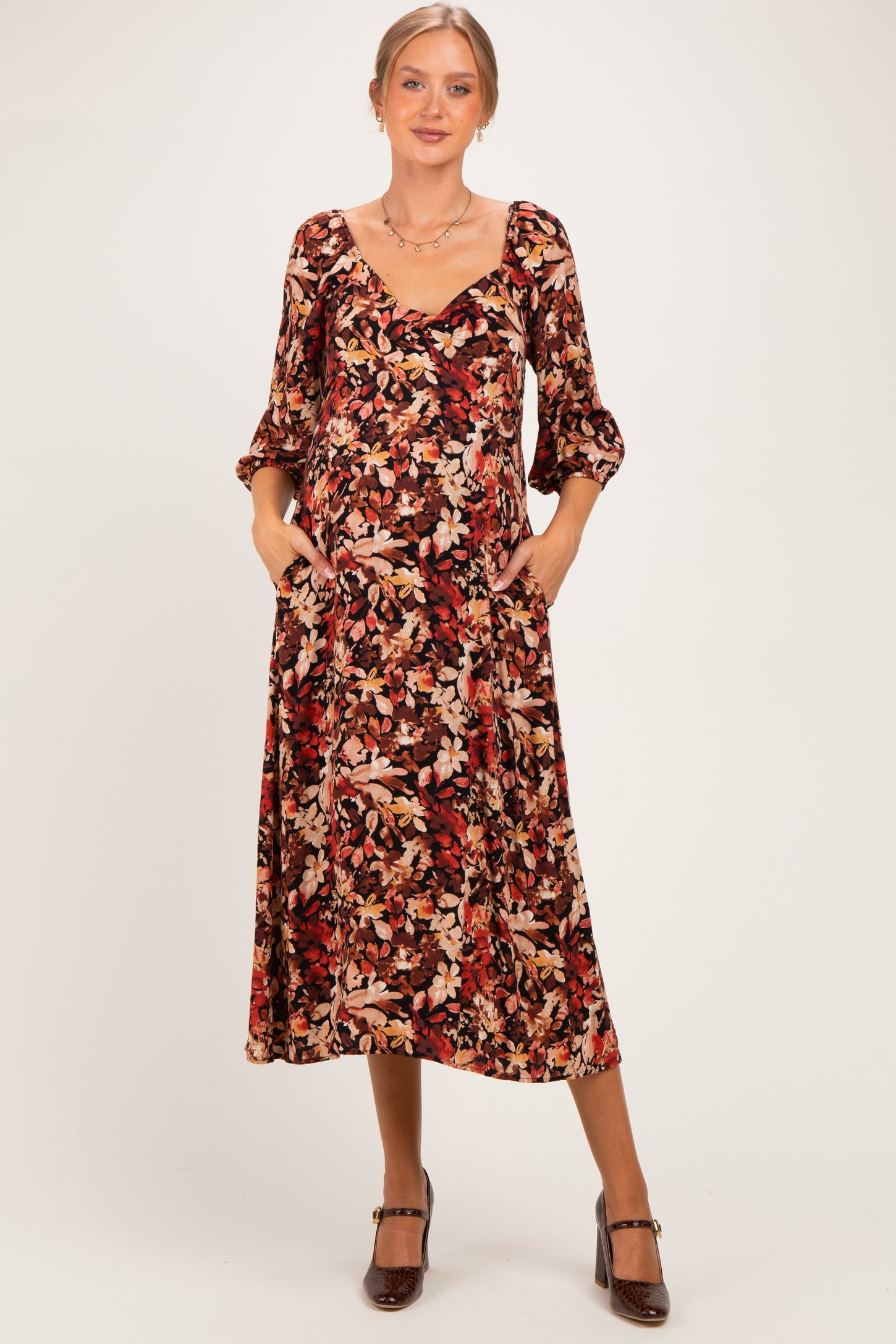 woman wearing a floral print maternity midi dress with three-quarter sleeves and pockets, showcasing her baby bump