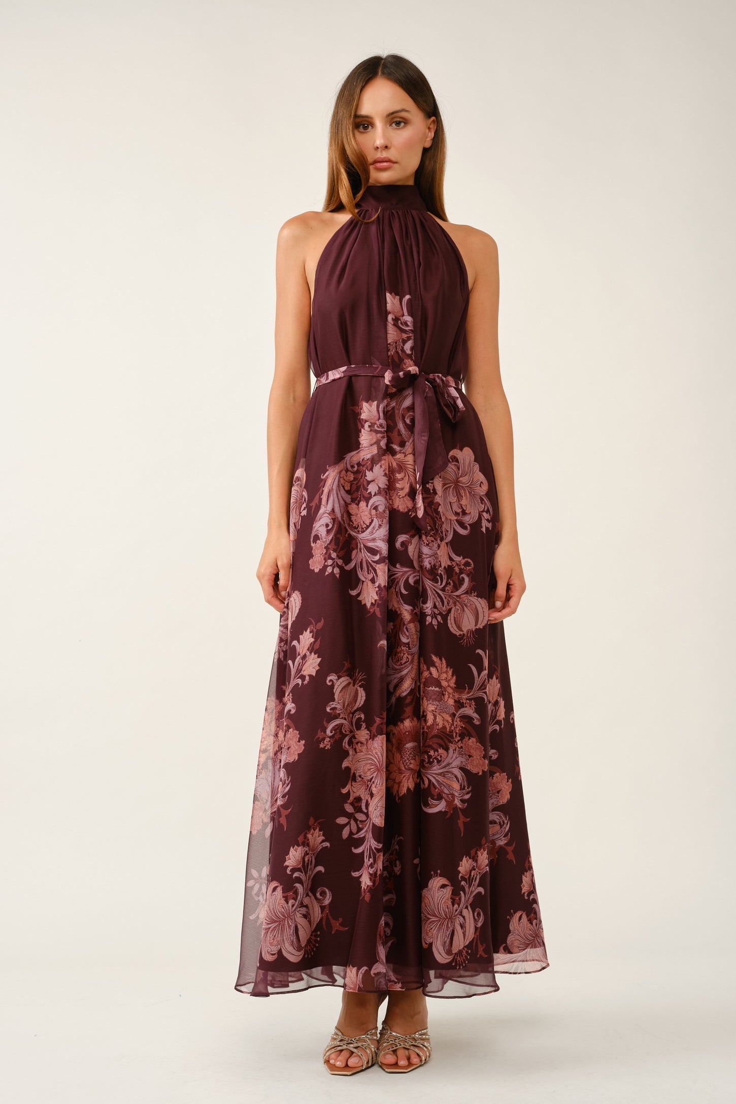 woman wearing a burgundy floral maxi dress with a halter neck and a tie waist detail