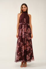 woman wearing a burgundy floral maxi dress with a halter neck and a tie waist detail