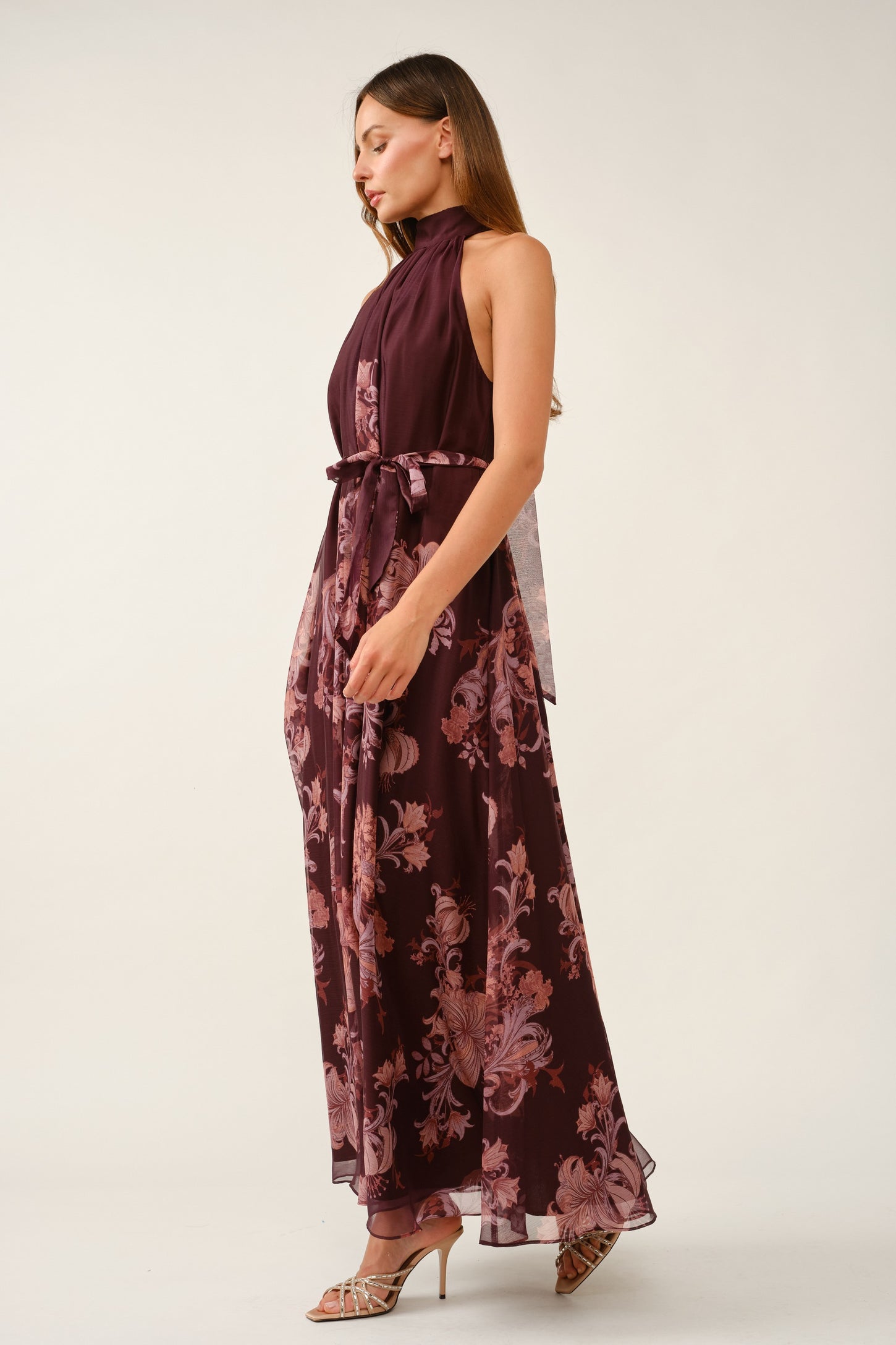 woman wearing a burgundy floral maxi dress with a high neck and tie waist detailing