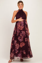 woman wearing a burgundy floral halter neck maternity maxi dress and holding her baby bump