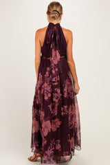 woman wearing a long purple floral maternity dress with a halter neck and flowing sheer skirt from the back
