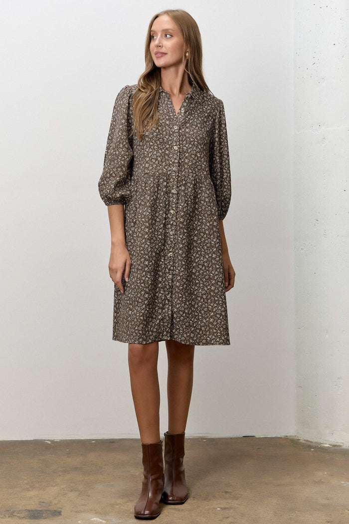woman wearing a brown floral button-up dress with puffed sleeves and standing on a concrete floor