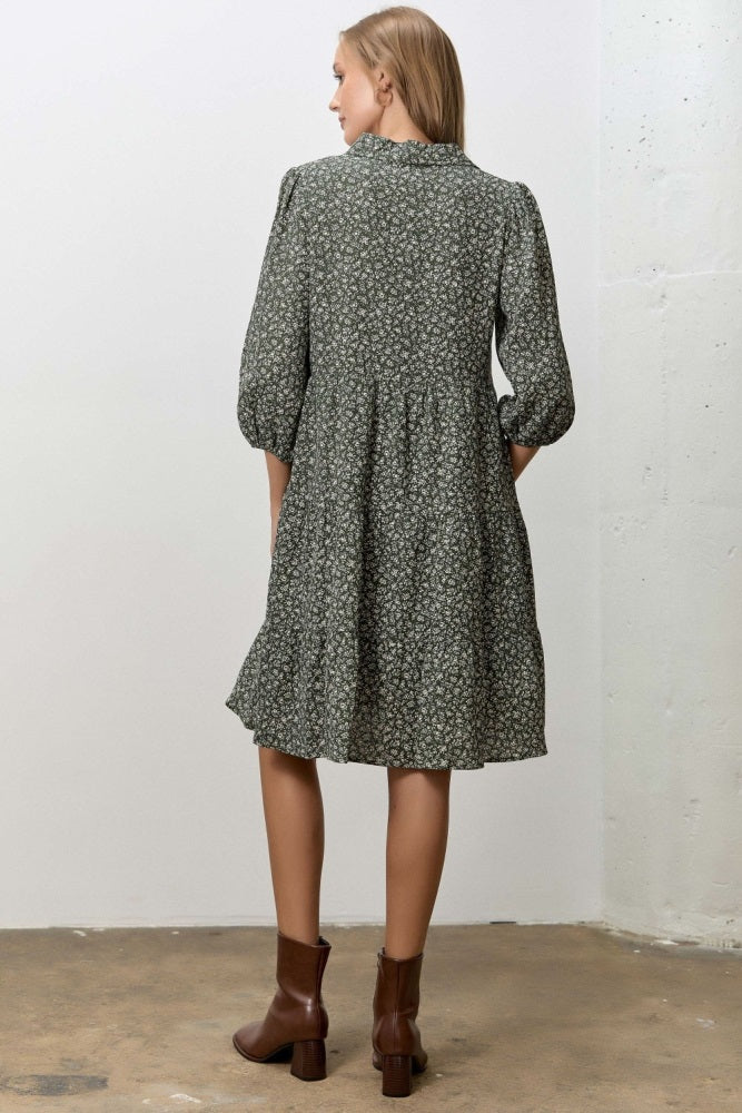 woman wearing a green floral short sleeve dress with a tiered skirt and brown ankle boots, view from the back