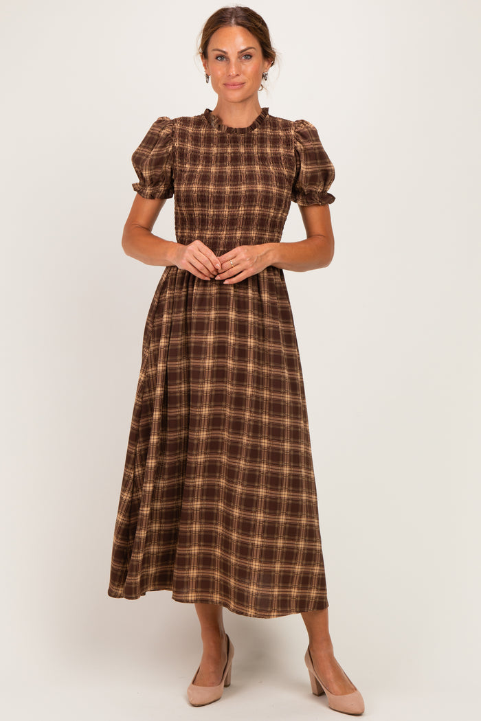 woman wearing a brown and tan plaid midi dress with puff sleeves and a cinched waist, standing in a neutral background
