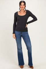 woman wearing a black long sleeve scoop neck top and flare jeans, standing with one hand on her hip