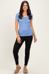 woman wearing a light blue short sleeve button-up top and black slim-fit pants, standing with one hand on her hip