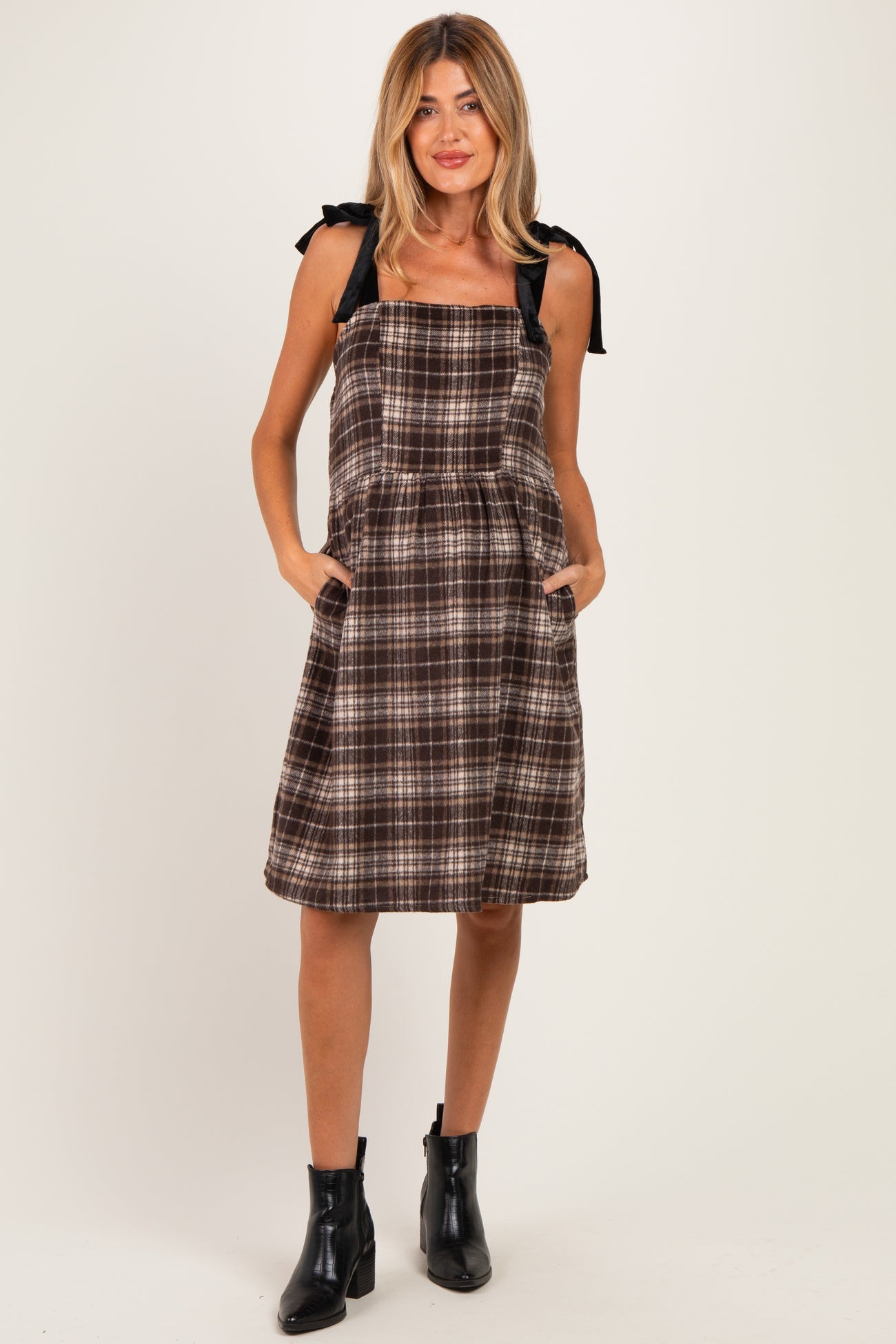 woman wearing a brown plaid maternity dress with tie straps and side pockets