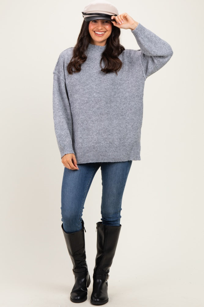woman wearing a gray oversized sweater, blue skinny jeans, and tall black boots with a cap on her head
