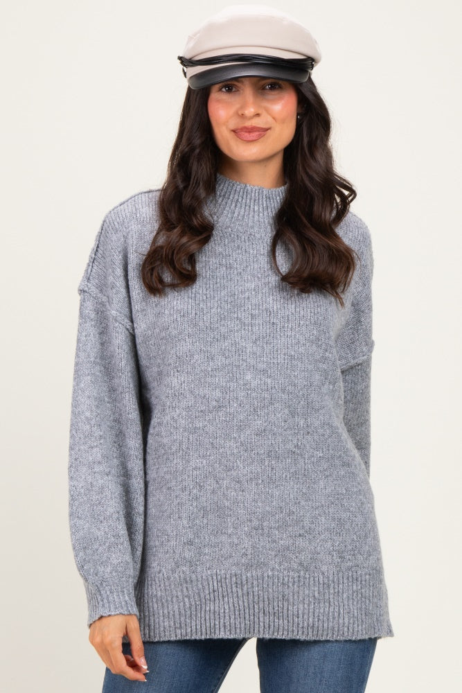 woman wearing a light gray oversized sweater with a high neckline and long sleeves, paired with a stylish cap