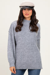 woman wearing a light gray oversized sweater with a high neckline and long sleeves, paired with a stylish cap