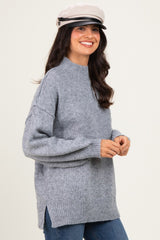 woman wearing a grey oversized sweater with a high neckline and side slits, paired with a stylish cap