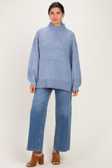 woman wearing a light blue oversized sweater with a mock neck and wide-leg jeans, standing in brown block-heeled sandals