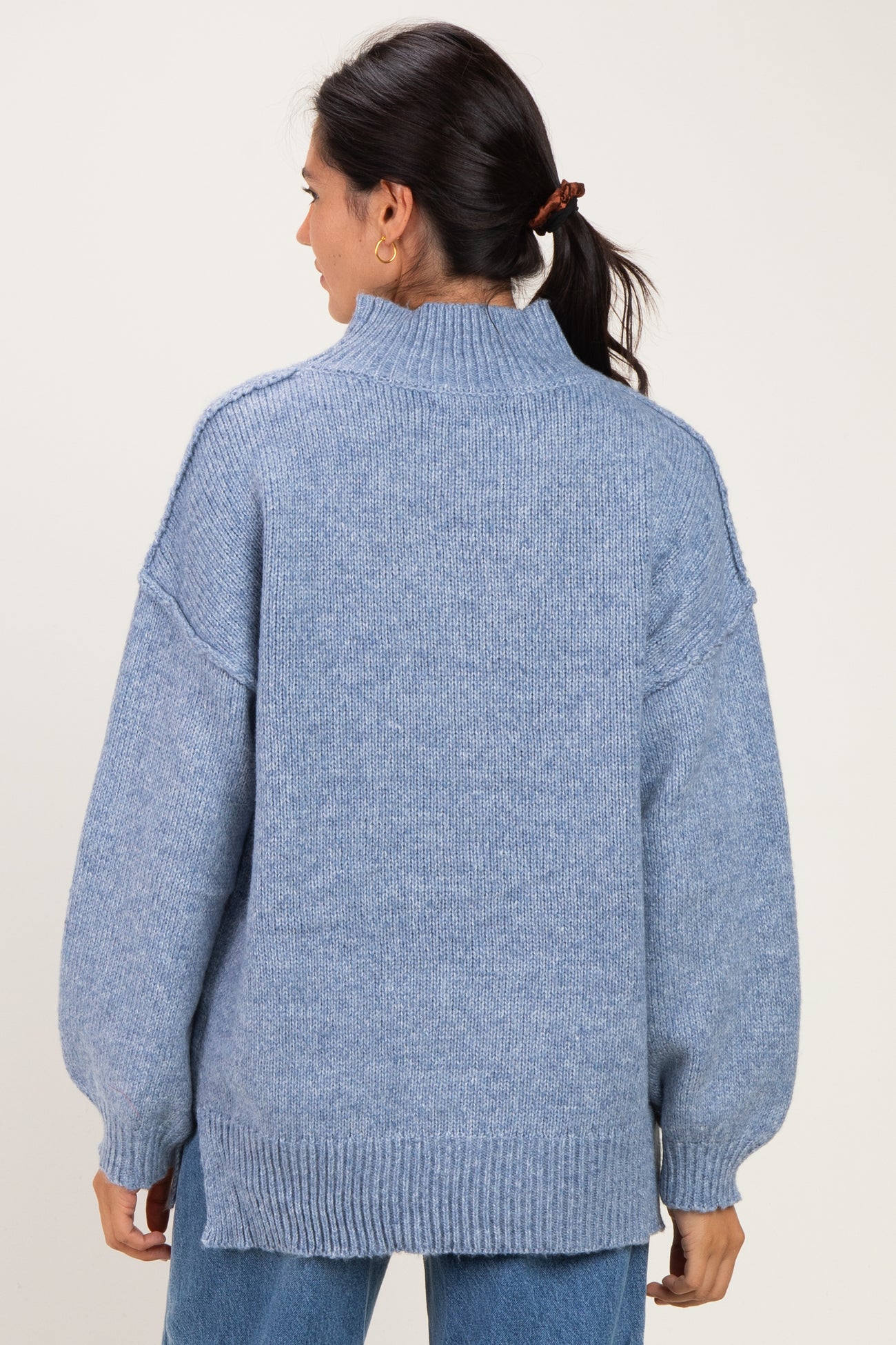 woman wearing a light blue oversized sweater with a high neck and drop shoulder sleeves