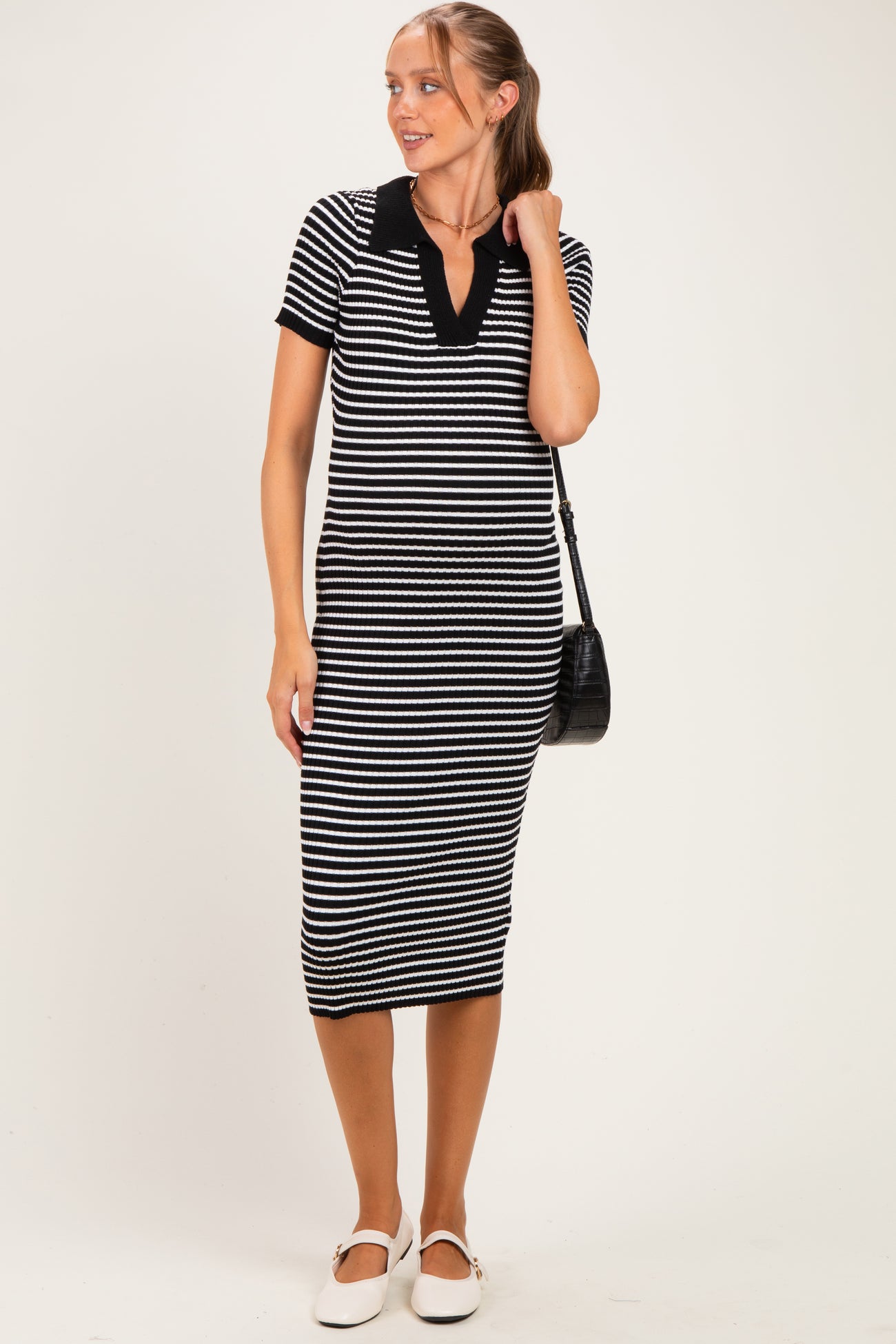 woman wearing a black and white striped maternity dress with short sleeves and a v-neck, holding a black bag