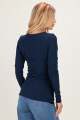 woman wearing a navy blue long sleeve fitted top with a scoop neckline and mid-back design, facing away from the camera