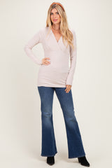 woman wearing a light pink long sleeve wrap top and flared jeans, standing with hands on hips
