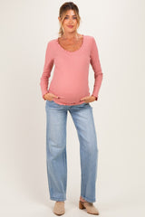 woman wearing a pink long sleeve maternity top with ruffle detailing and jeans, holding her baby bump