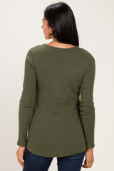 woman wearing a dark olive green ribbed long sleeve top, seen from the back with a rounded hem