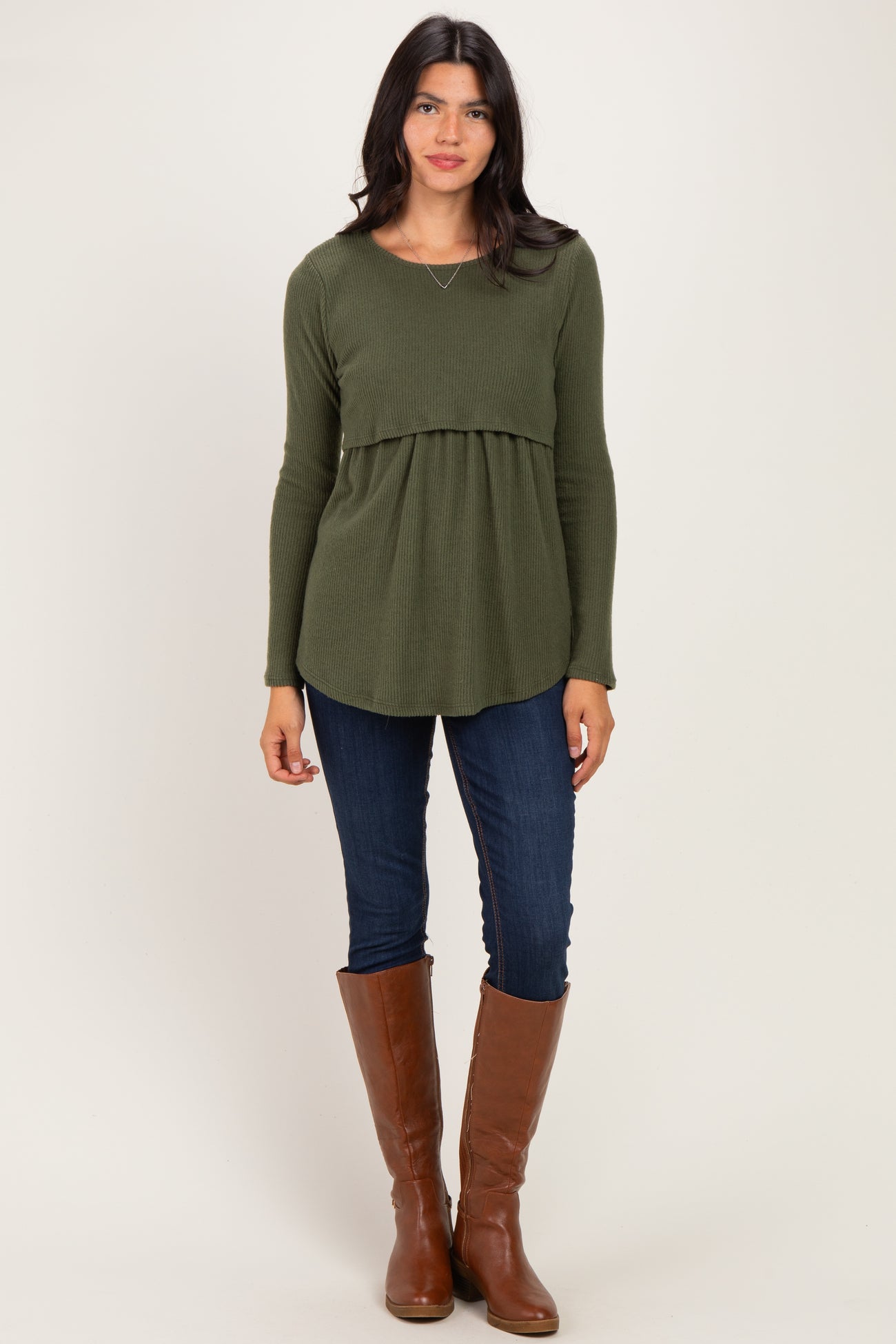 woman wearing an olive green peplum top with long sleeves, paired with dark skinny jeans and tall brown boots