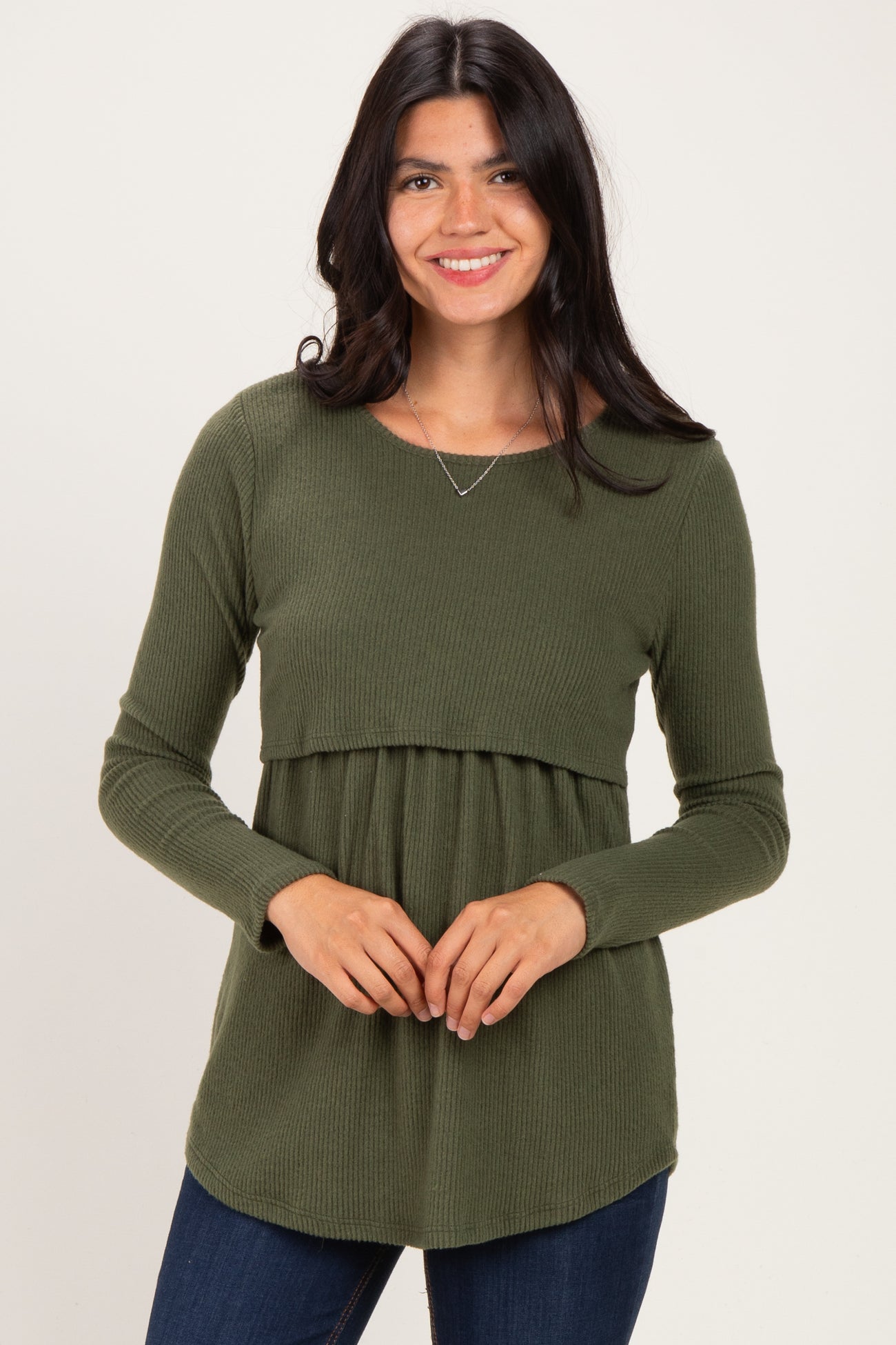 woman wearing a dark green long sleeve ribbed top with a fitted bodice and flowy bottom, smiling at the camera