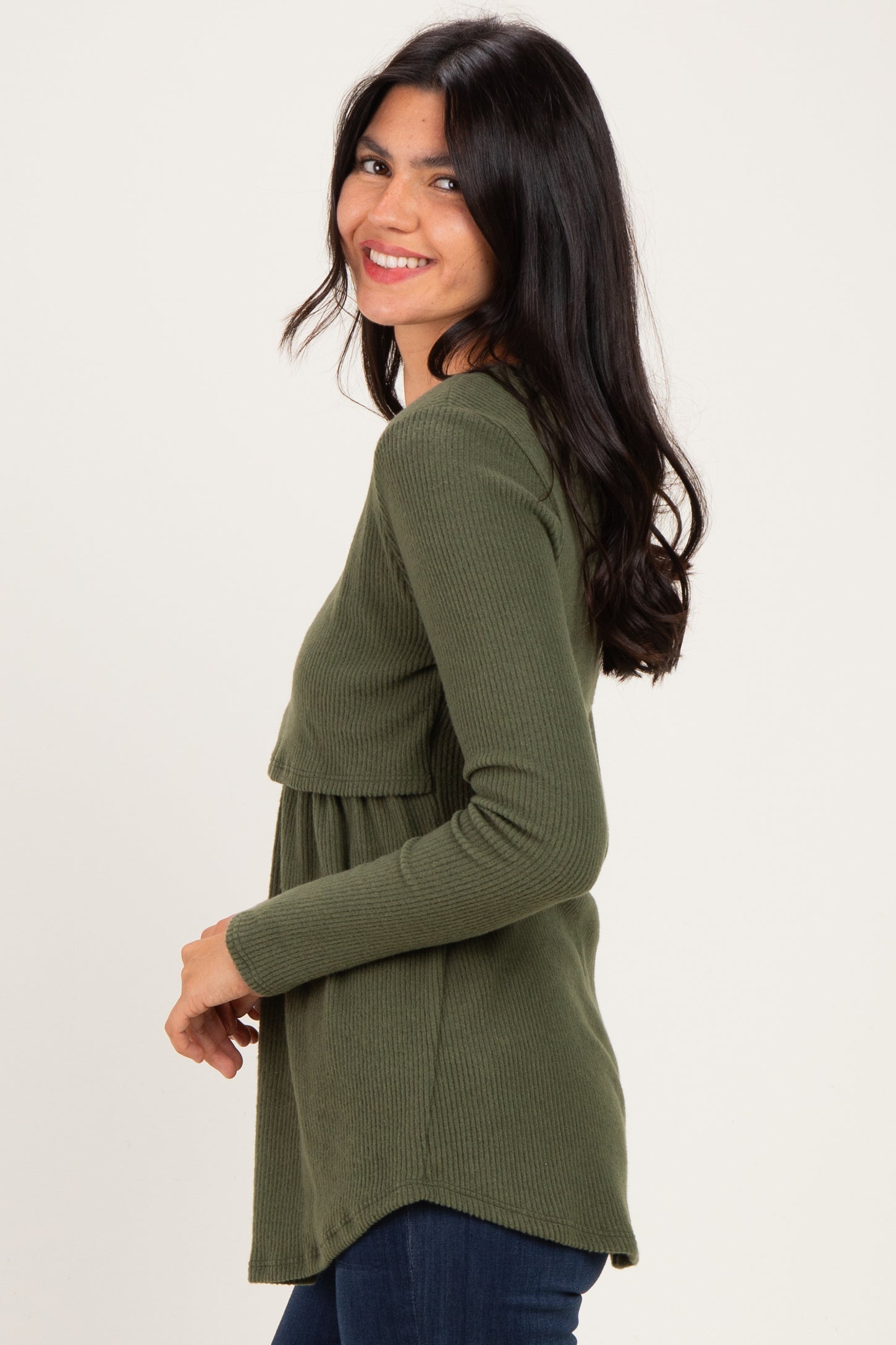 woman wearing a green ribbed long sleeve top with a layered design and smiling at the camera