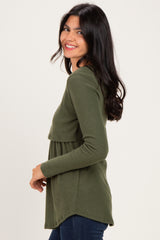 woman wearing a green ribbed long sleeve top with a layered design and smiling at the camera