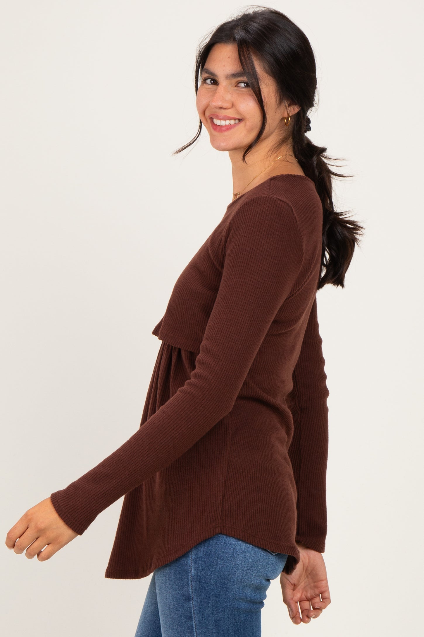 woman wearing a brown ribbed long sleeve top with a relaxed fit and flared hem, smiling and posing sideways