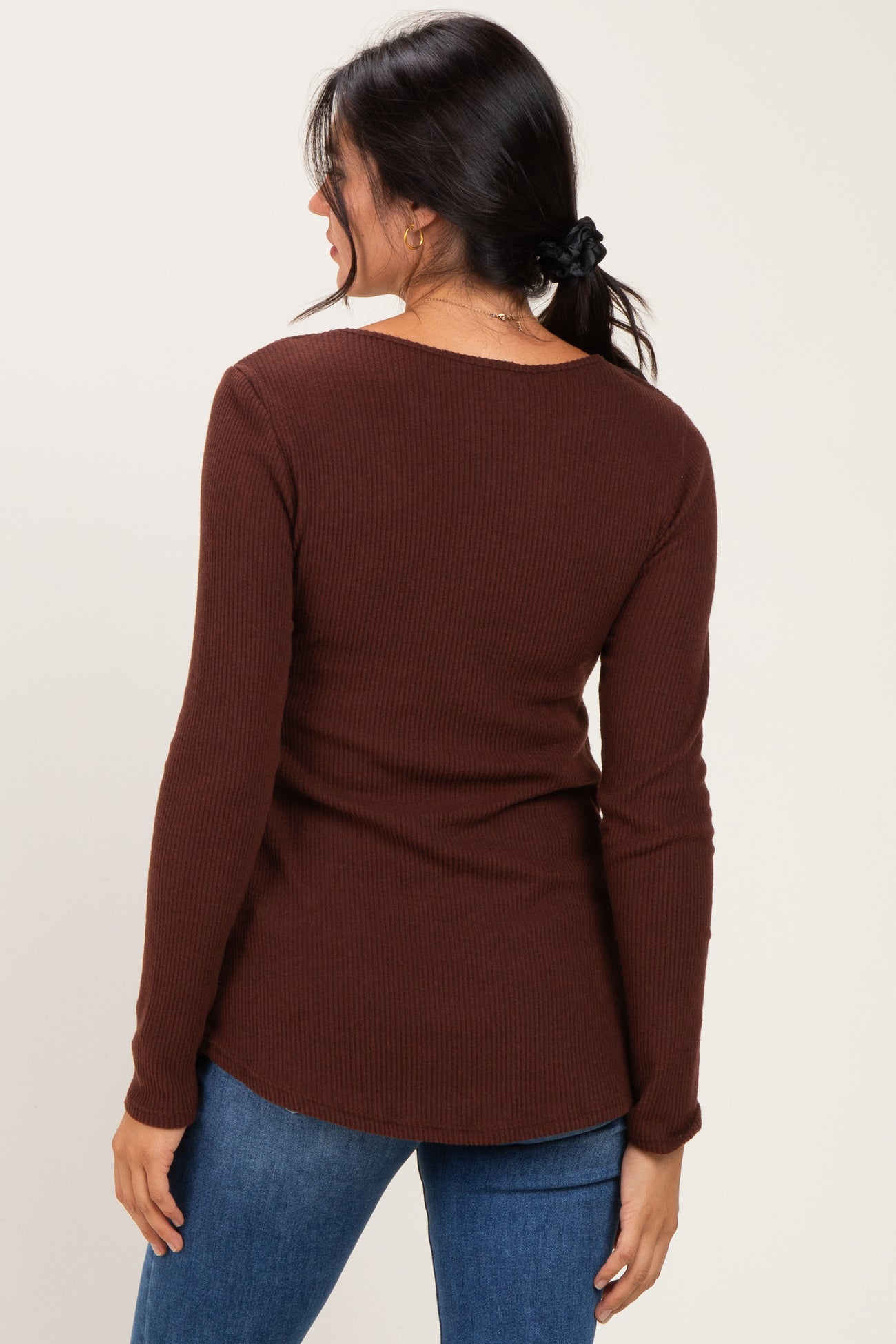 woman wearing a brown ribbed long sleeve top with a slight scoop back and paired with blue jeans