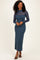 woman wearing a dark teal ribbed midi dress with sheer long sleeves and a high neckline, standing and smiling