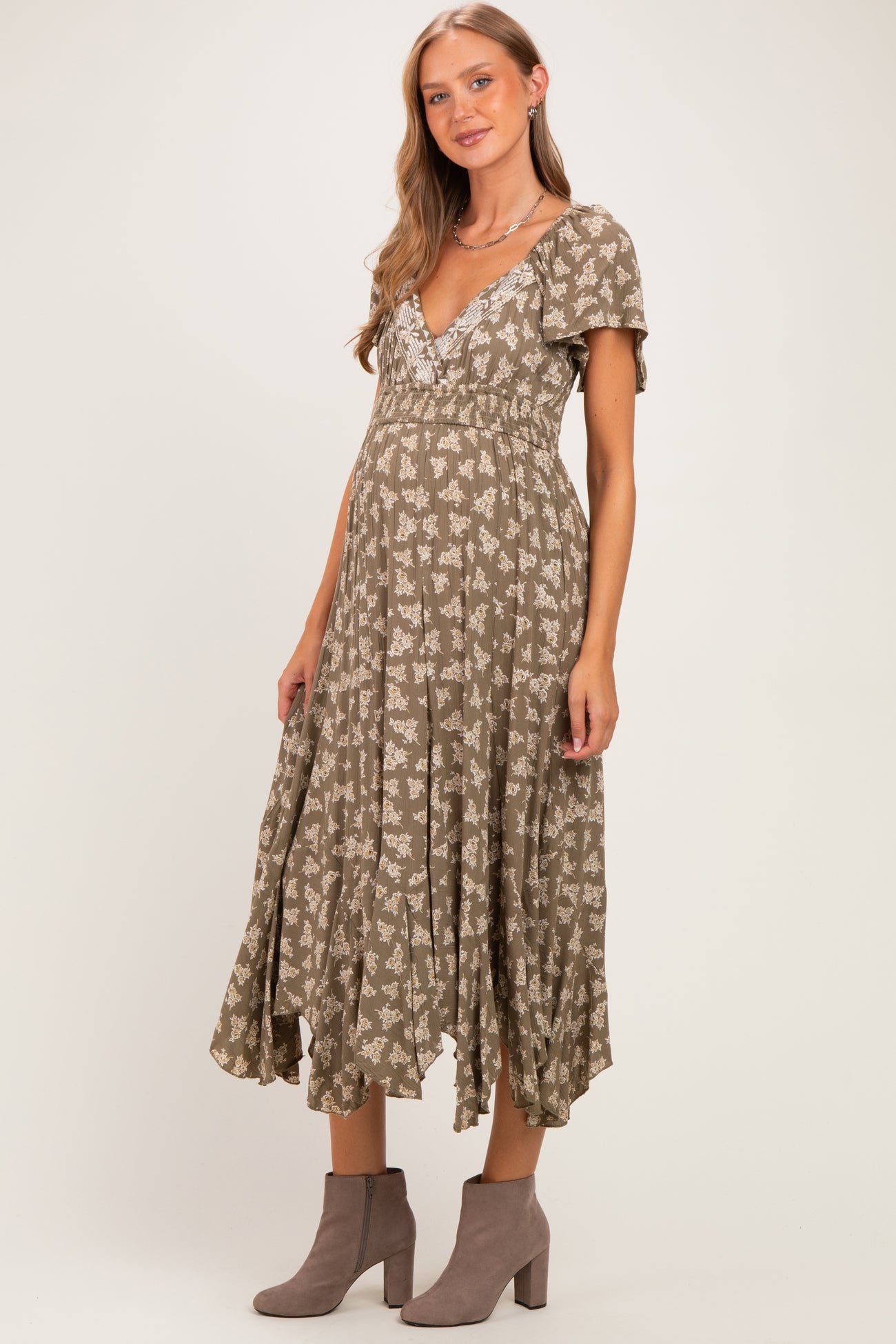 woman wearing a sage green floral maternity dress with short sleeves and a flowy skirt, showing her baby bump