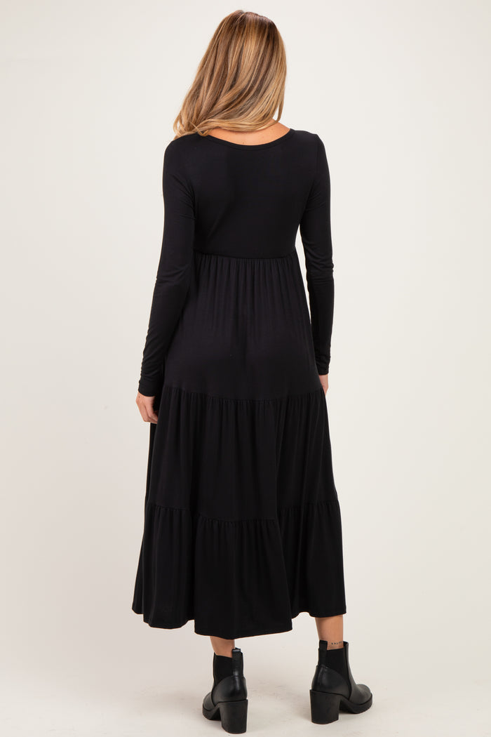 woman wearing a black long sleeve maternity dress with a tiered skirt and a relaxed fit, standing with her back to the camera