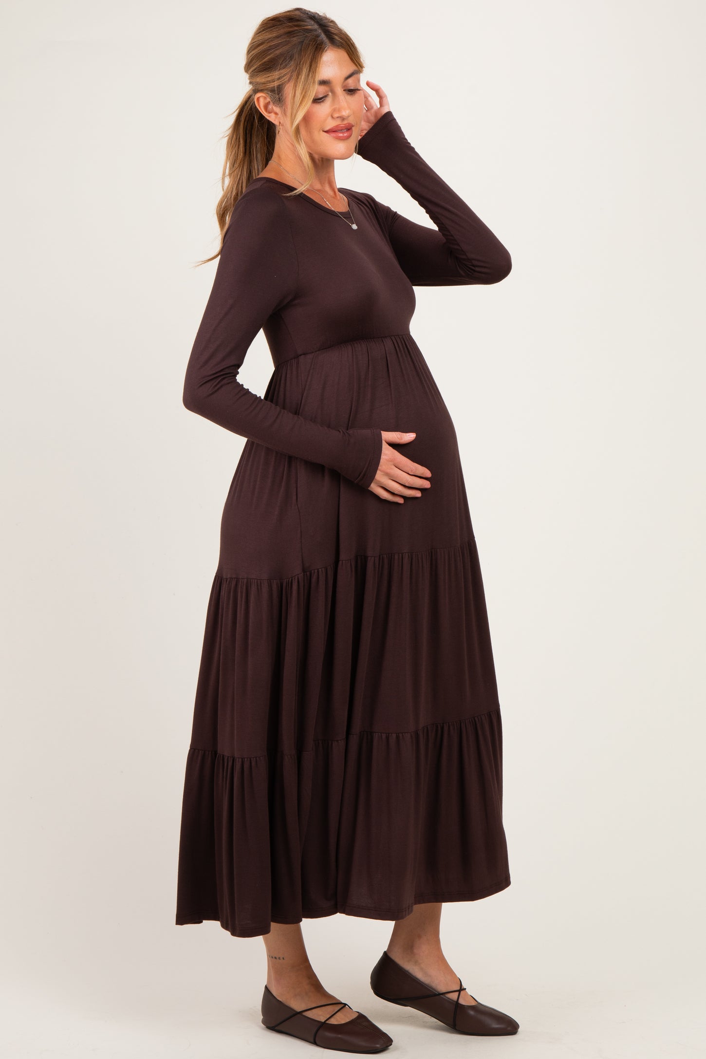 woman wearing a dark brown long sleeve maternity maxi dress and cradling her baby bump