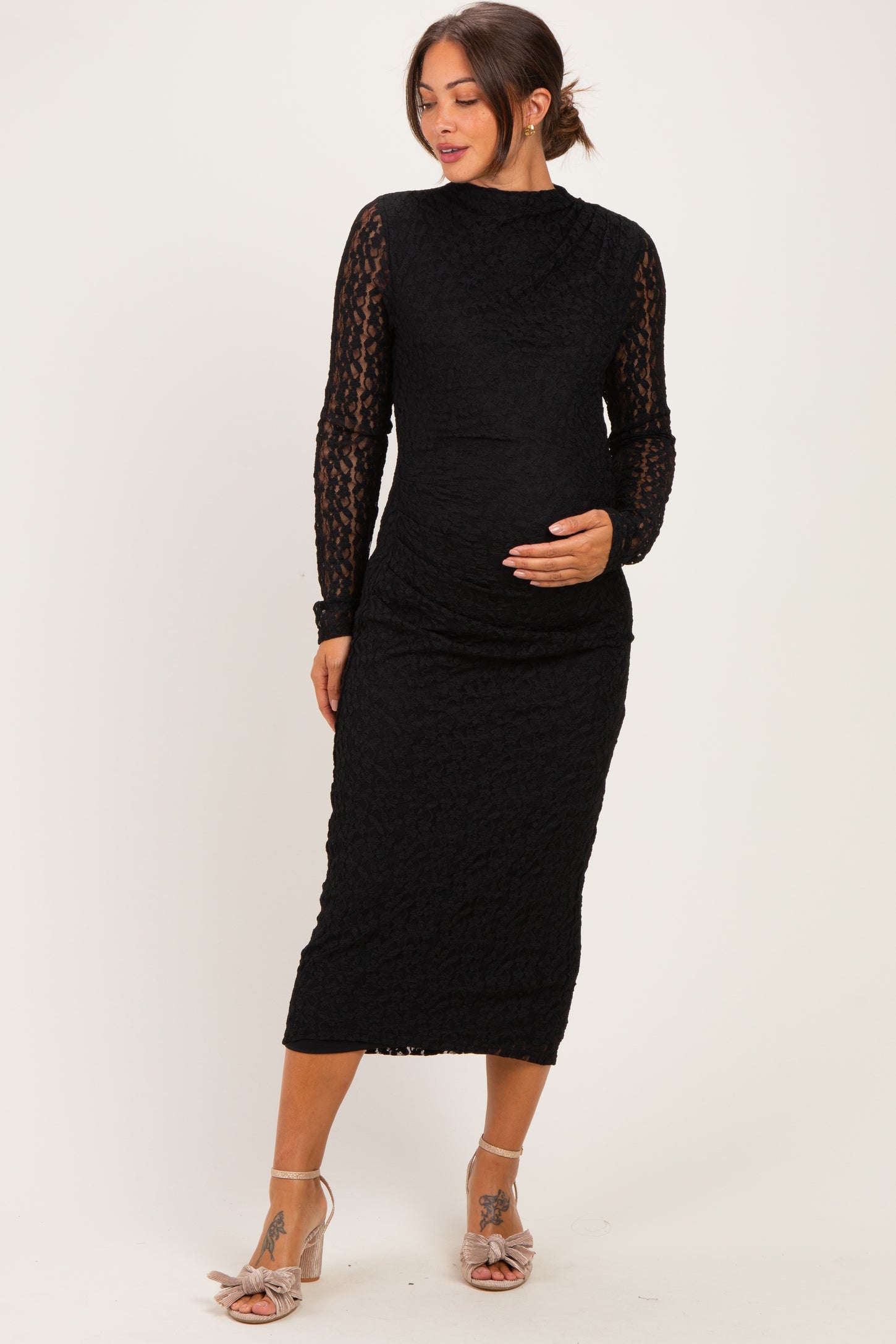 woman wearing a black lace maternity dress with long sleeves and a fitted silhouette, cradling her baby bump