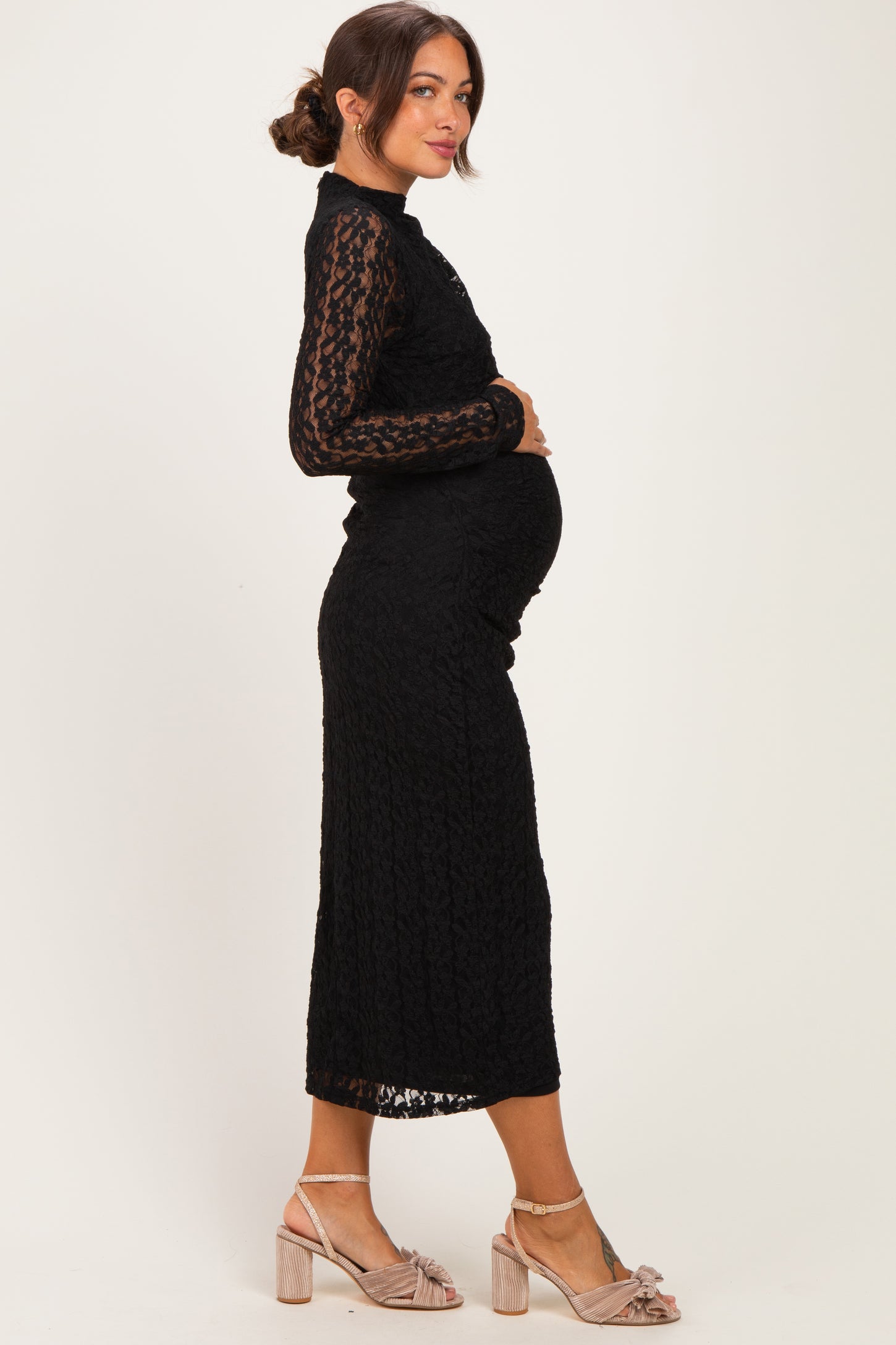woman wearing a black lace maternity dress and showing her baby bump, styled with heels