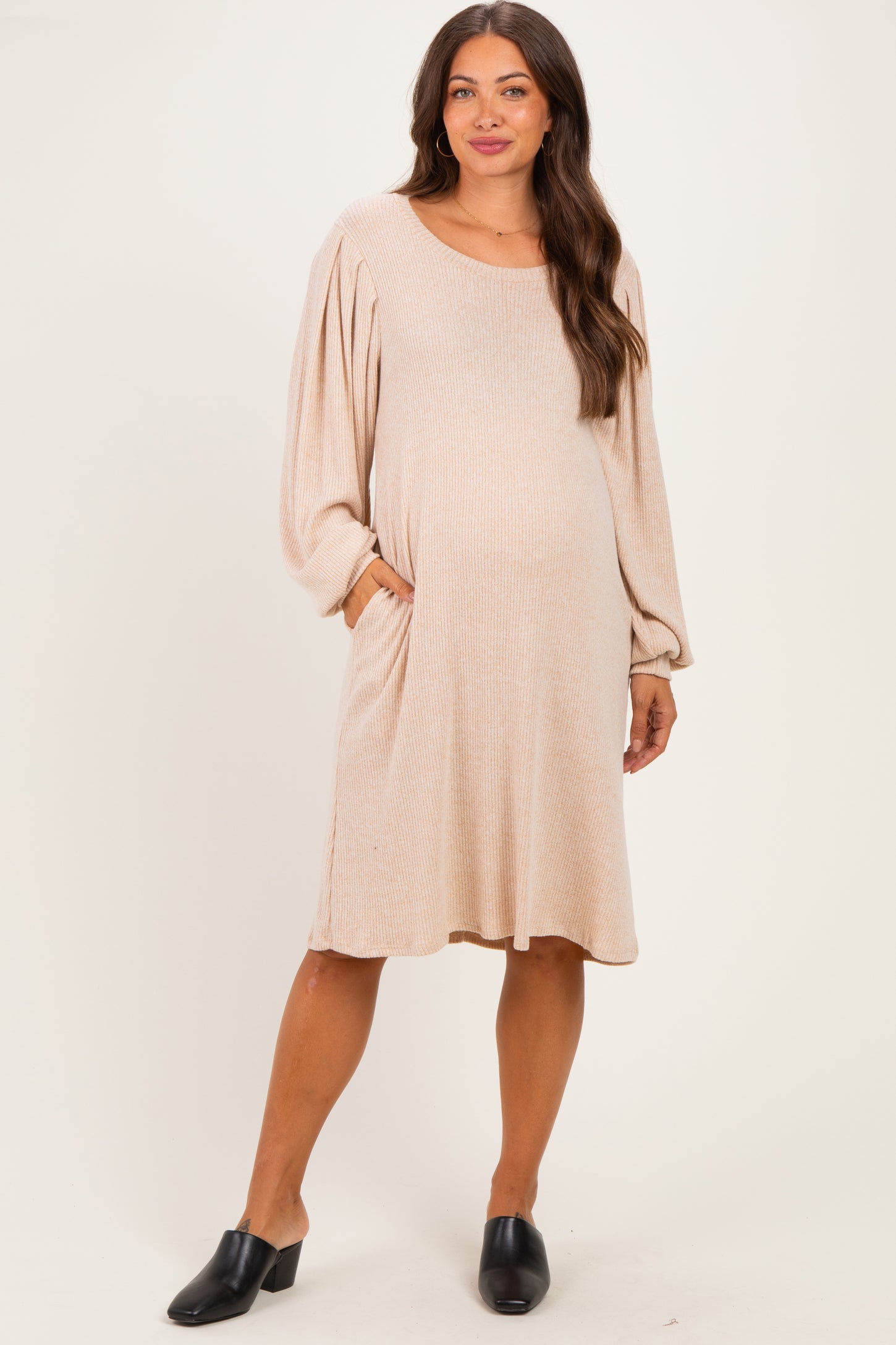woman wearing a beige maternity dress with long puff sleeves and pockets, showcasing a visible baby bump