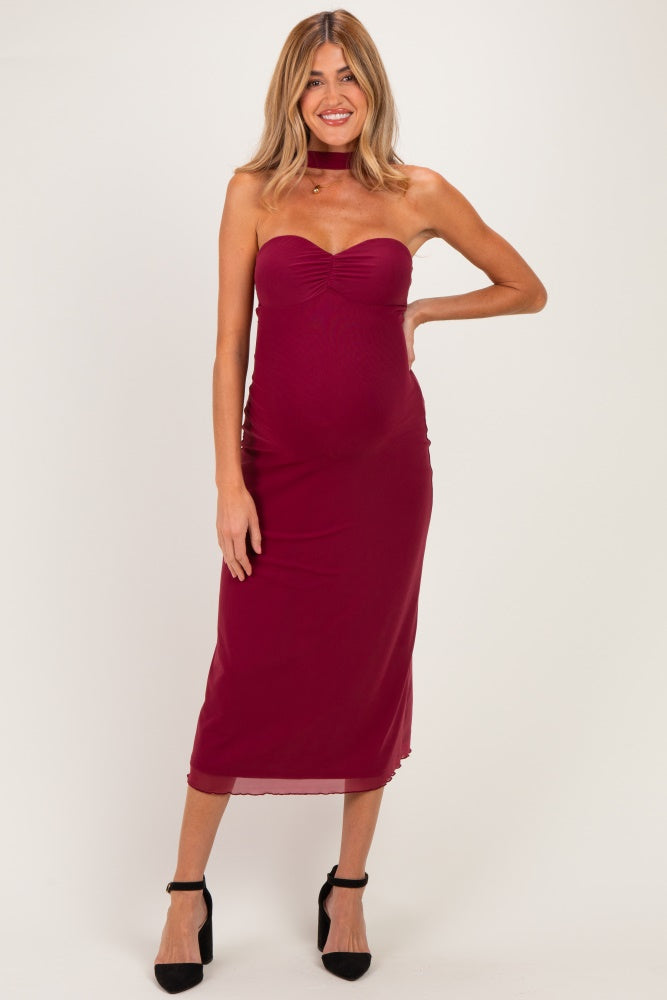 woman wearing a burgundy strapless maternity dress with a fitted silhouette and a choker detail, showing her baby bump