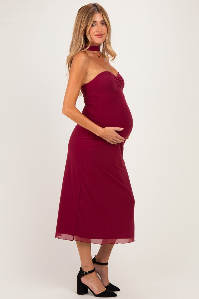 woman wearing a burgundy maternity dress with a fitted bodice and flowing skirt, showing her baby bump