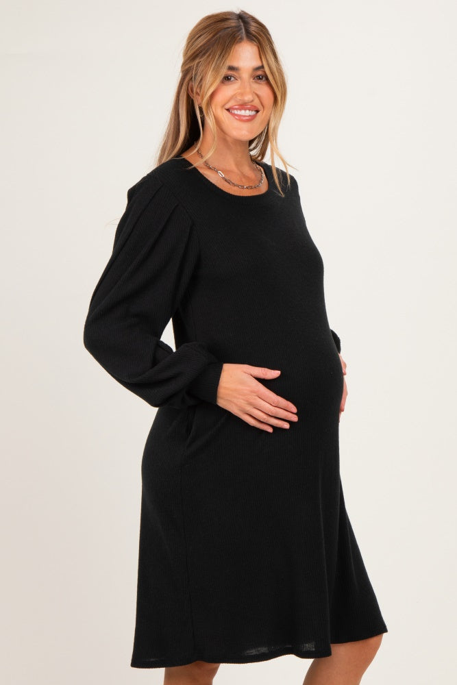 woman wearing a black long sleeve ribbed maternity dress and holding her baby bump