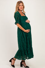 woman wearing a dark green lace maternity dress with short sleeves and a tiered hem, holding her baby bump