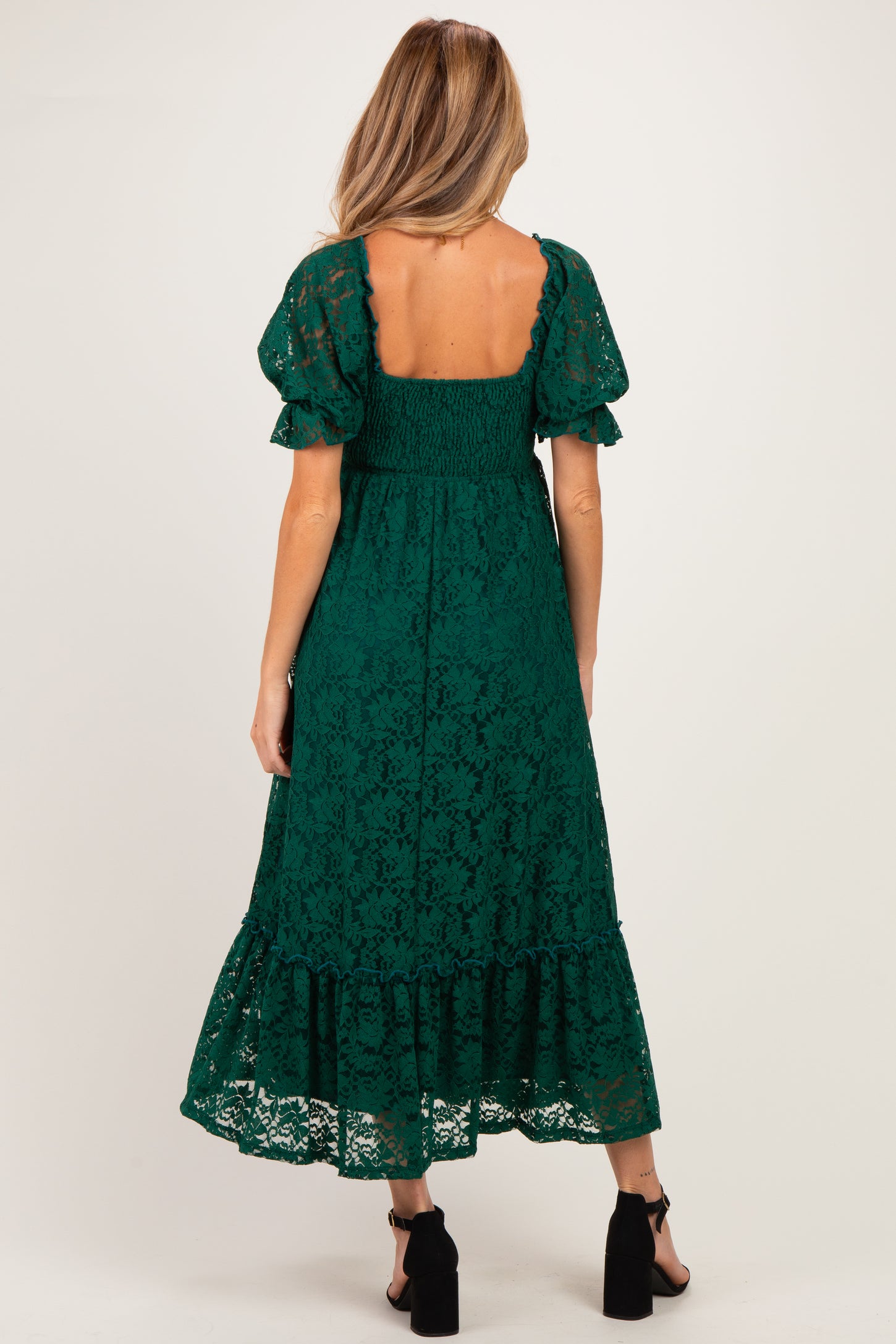 woman wearing a green lace maternity dress with puff sleeves and a tiered skirt, showcasing a smocked back design